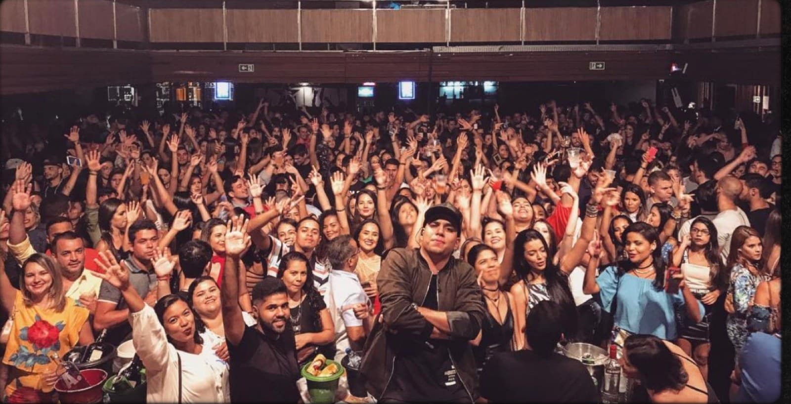 PV Mello no meio de uma casa de show lotada, com o público de mãos erguidas ao redor