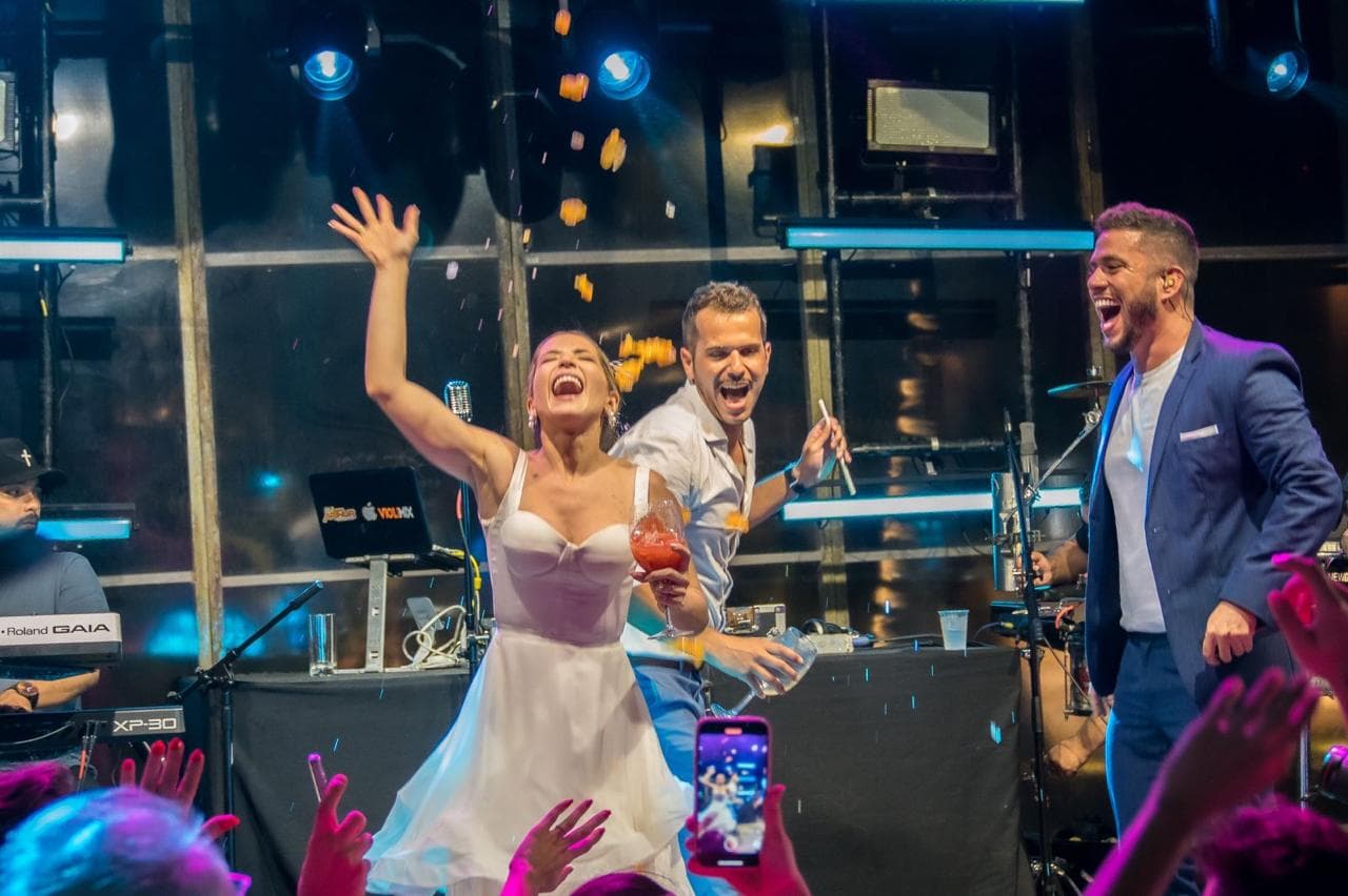 Noivos comemorando no palco ao lado de PV Mello durante a festa