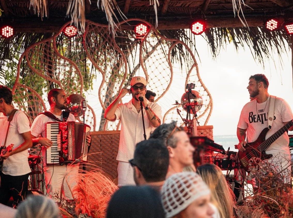 Banda de PV Mello tocando em palco à beira-mar no fim da tarde